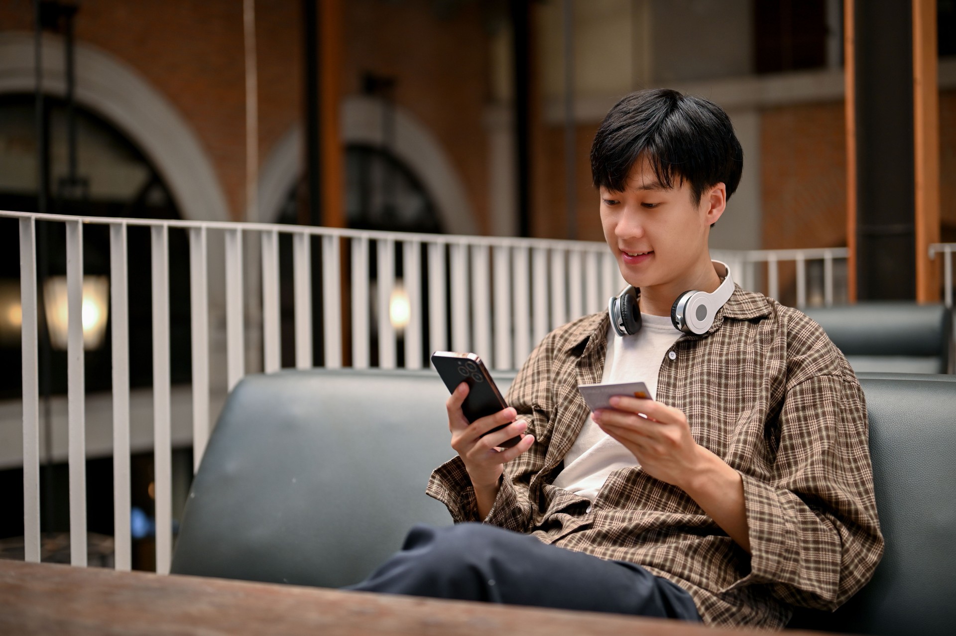 Happy Asian man holding a smartphone and a credit card, using mobile banking application